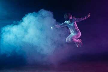 Fototapeta na wymiar Fencer jumping while exercising with rapier on black background with lighting and smoke
