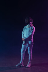 Swordswoman in fencing mask and suit holding rapier and looking away on black background