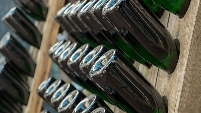 Wooden racks with filled green bottles of champagne during traditional bottle fermentation waiting for the next manual bottle rotation to proceed with the maturation process. 
