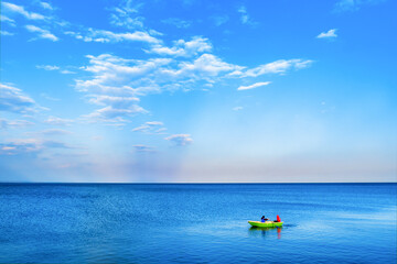 A company of young people is sailing in a boat. A green boat is sailing in the blue sea against the background of cloudy clouds.