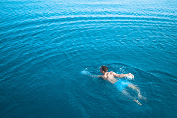 The young guy swims beautifully in the blue water. Handsome man crawls in the blue sea. The guy is swimming in the beautiful blue sea.