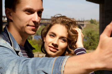 Two young people man and woman wearing jeans outdoors doing selfie