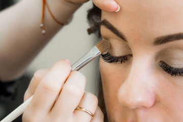 brush with eyeshadow in the hands of a makeup artist at the eyes of a girl in a beauty salon