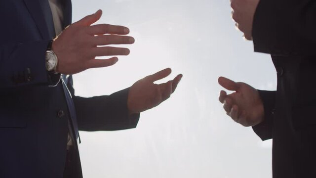 Mid-section slowmo of unrecognizable businessmen in suits gesticulating and discussing work outdoors on sunny day