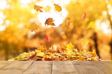 Naklejka na ściany i meble Wooden surface and falling autumn leaves outdoors