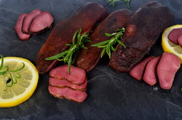 smoked pork tongue on a black stone and decorated with rosemary and lemon