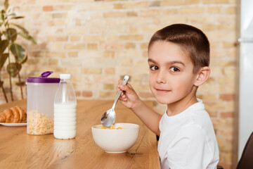 Side view of boy looking at camera while eating cereals in kitchen