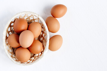 Brown chicken eggs in a straw basket on white wooden background. Top view with copy space.