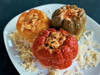 Stuffed bell peppers. Three cooked stuffed peppers on a white plate. Close-up. Juicy Peppers Recipe. Delicious multi-colored peppers stuffed with minced meat and rice. 