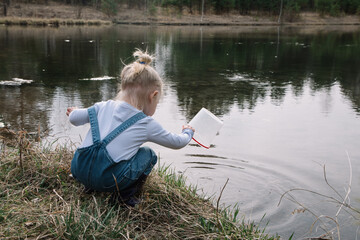 Little girl in rubber boots catches and feeds fish on the river in a jar