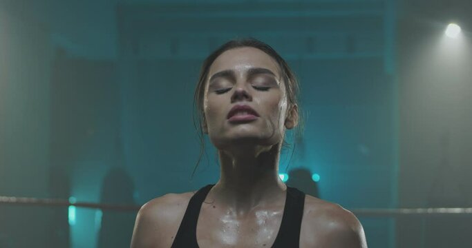 Close up of Caucasian young tired sweaty woman in sportswear standing in fron of camera and wiping her forehead with hand. Boxing training concept. Spotswoman after working out.