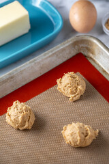 Peanut butter dough balls on a silicon baking mat, with baking ingredients