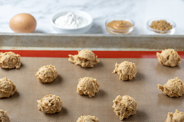 Peanut butter dough balls on a cookie sheet beside baking ingredients