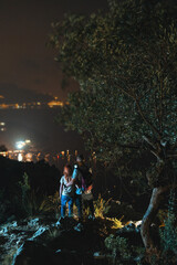 Obraz premium Two tourists on top of the mountain. Climbing, hiking trail. View of the night city. Romantic setting. Couple in love. Active lifestyle. The best view. vertical photo. Vacation. Nerano, Italy