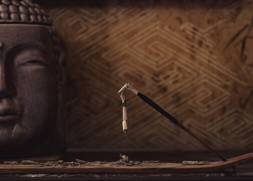 Burning Single Incense Stick For Meditation With Buddha On The Background.