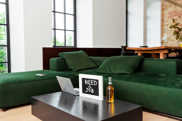 laptop near chalkboard with need a job lettering and bottle of beer near modern sofa