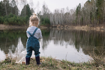 Fototapeta na wymiar Little girl in rubber boots catches and feeds fish on the river in a jar