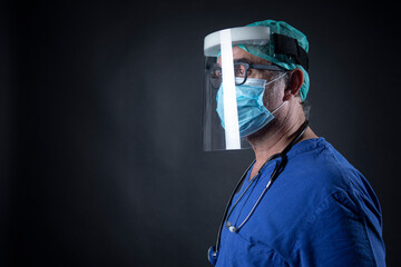 medico con cuffietta,  mascherina e schermo in plexiglass e camice blu isolato su sfondo nero