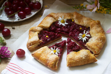 Sweet pie galette with juicy berry filling, berries and wild flowers on a wooden background. Rustic style.