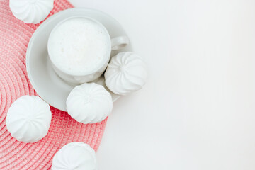 Cup of cappuccino and white zephyr on white and pink background. Top view with copy space