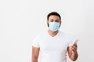 african american man in medical mask holding smartphone near white wall