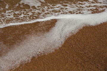 Sea water and the white foam on the beach in Golden sunshine, yellow sand