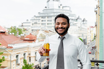 smiling african american man holding bottle of beer on balcony