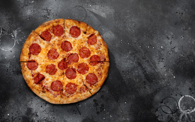 Pepperoni pizza on black concrete background. Top view with copy space. Tasty sliced pepperoni pizza