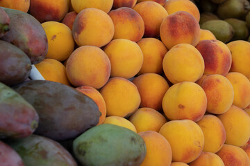 A counter with a nested pile of ripe peaches and mangoes. Selective focus.