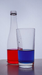 bottle and glass. In which the red and blue liquids are poured on a white background