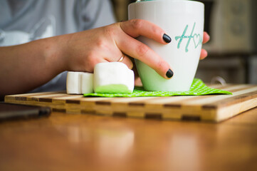 Black coffee with white melting marshmallows, sprinkled with chocolate chips with a black straw in a white mug with the inscription house in female hands.