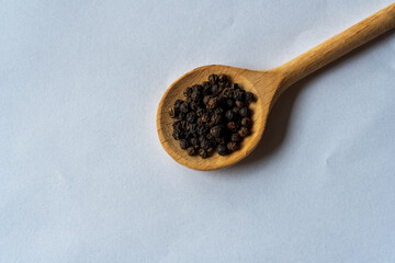 Closeup black pepper seeds or peppercorns ( dried seeds of piper nigrum) in wooden spoon isolated on white background. top view. Flat lay.