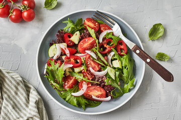 Healthy vegetable salad of fresh tomato, cucumber, pepper, onion, lettuce, arugula, flax seeds and olive oil on plate. Diet menu, top view	