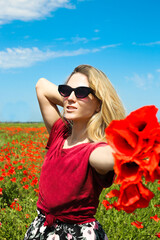 Beautiful young woman walking at the poppy meadow. Young girl in the long red dress at the poppy field at summer time. Happy tourist woman traveller.