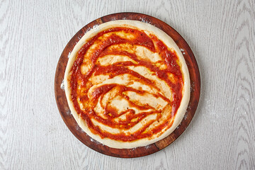 Pizza dough, 3rd step of spread the pizza dough with tomato sauce on wooden board isolated on gray background. (How to make Pizza?) The basics of pizza making process, top view