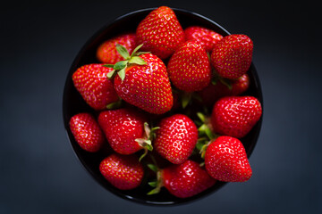 Fresh ripe strawberries in a black bowl isolated on neutral background, top view.