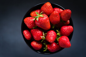 Fresh ripe strawberries in a black bowl isolated on neutral background, top view.