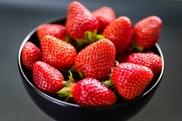 Fresh ripe strawberries in a black bowl isolated on neutral background, top view.