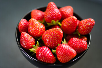 Fresh ripe strawberries in a black bowl isolated on neutral background, top view.