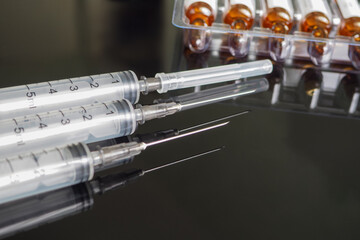 disposable syringes and ampoule packages with medical products close up on a dark mirror background