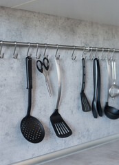 Different kitchen tools for cooking hanging on the gray wall.
