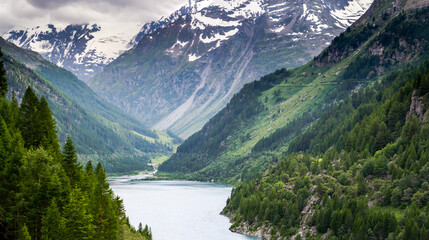 Naklejka na ściany i meble Paesaggio alpino. Alta montagna. Lago di Beauregard. Artificiale. Vista verso il sentiero e il fiume che arriva alla sorgente. Valle d'Aosta. Italia