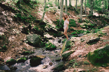 Happy tourist girl teenager in forest near to the cold fresh stream river at the waterfall Shypit, cascade in Pylypets in the forest. Carpathian Mountains