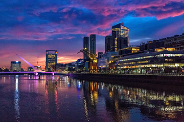 Fototapeta na wymiar Puerto Madero Bridge and city by the river, during sunrise, with colorful clouds. 