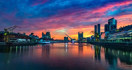 Fototapeten Puerto Madero Bridge and city by the river, during sunrise, with colorful clouds.  © Bernardo Galmarini