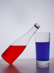 composition from a bottle and glasses with multicolored liquid on a white background. The bottle rests on a glass