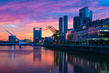 Fototapeta na wymiar Puerto Madero Bridge and city by the river, during sunrise, with colorful clouds. 