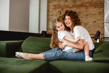 happy daughter hugging cheerful and curly mother