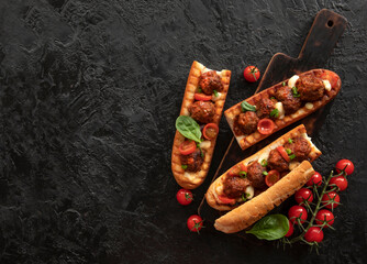 sandwich with meatballs on a baguette, with melted cheese, tomato sauce, parsley and Parmesan cheese on top.  Italian meatballs baked in a baguette on a black background. The view from the top.  - 353679007