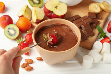 Woman dipping strawberry in chocolate. Delicious chocolate fondue
